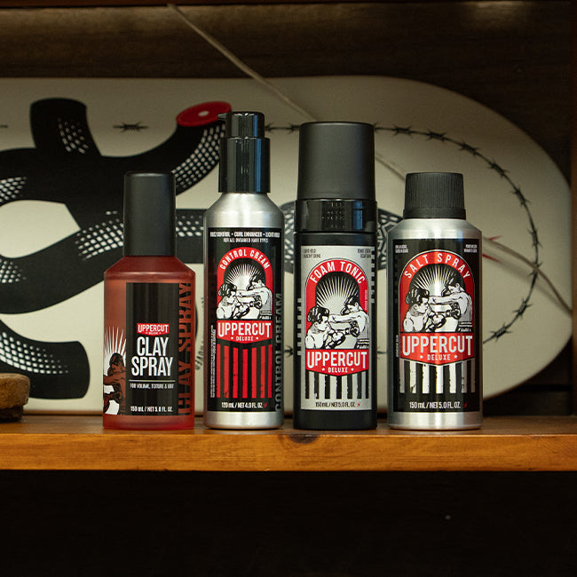Uppercut Deluxe Clay Spray, Control Cream, Foam Tonic and Salt Spray sitting on a shelf with a skateboard behind them