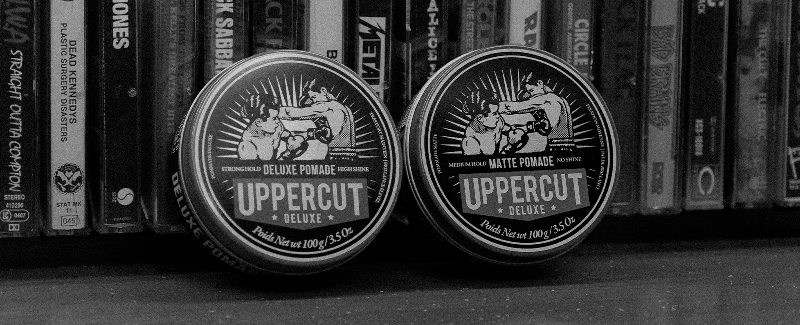 Uppercut Deluxe Matte Pomade and Deluxe Pomade tins leaning against cassettes