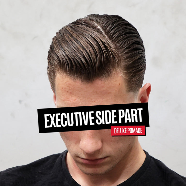 A man wearing a styled side-parted pomade hairstyle, shown from the chest up against a light textured wall. A black banner across the eyes reads 'EXECUTIVE SIDE PART' and a small red badge reads 'DELUXE POMADE'.